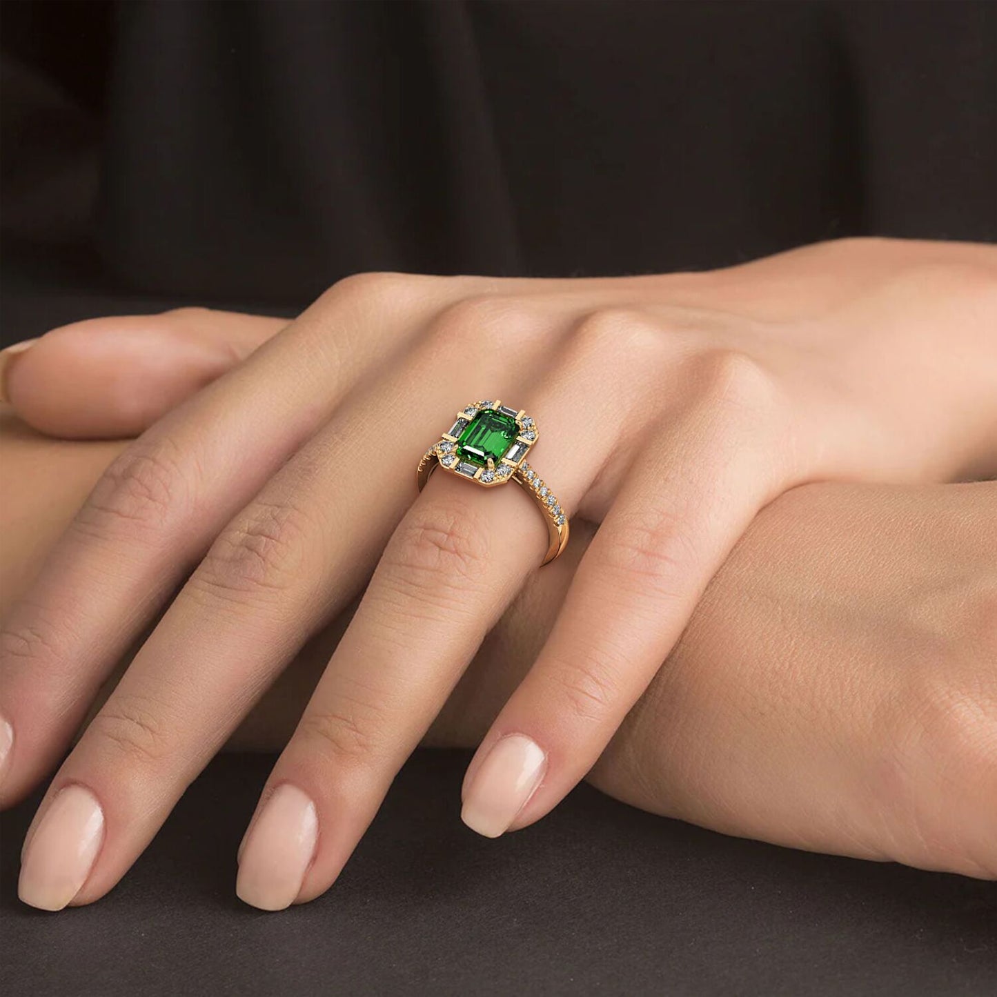 A hand wearing a gold ring with a large emerald-cut green YAG center surrounded by small diamonds, set against a dark background.