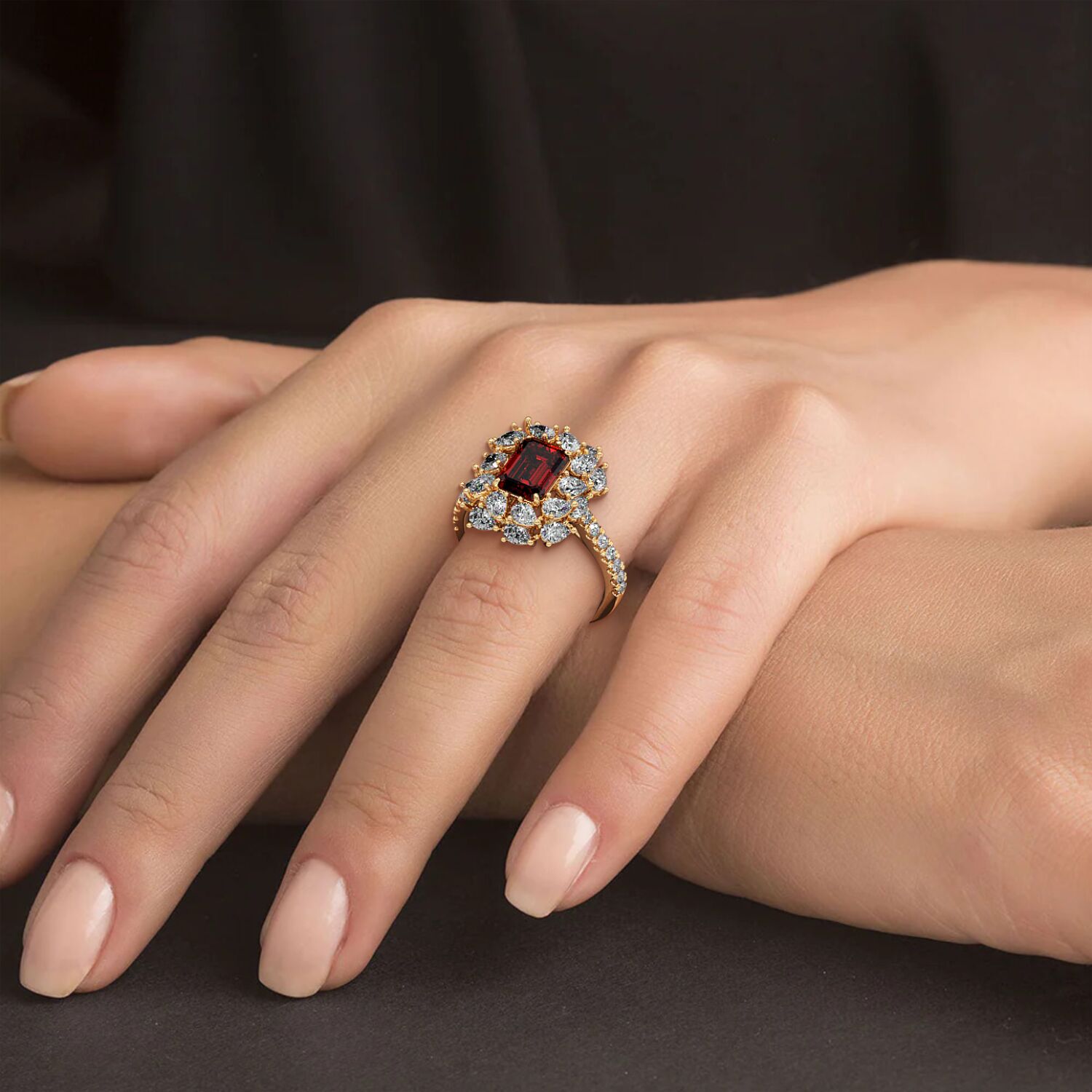 Hand wearing a 14k gold ring with a 2.50CT red ruby encircled by diamonds against a dark, luxurious background