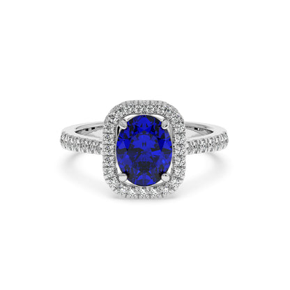 White gold ring with a deep blue oval 2.50CT sapphire surrounded by a halo of sparkling diamonds, with additional diamonds along the band.