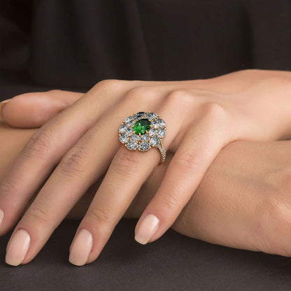 A hand wears a 14k gold ring featuring a 2.50CT oval green YAG surrounded by sparkling diamonds, exuding elegance against a dark background.