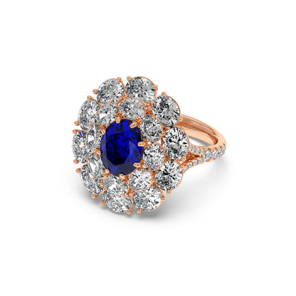 A 14k rose gold ring with a 2.50CT oval blue sapphire surrounded by white diamonds in a floral pattern, exuding elegance and luxury.