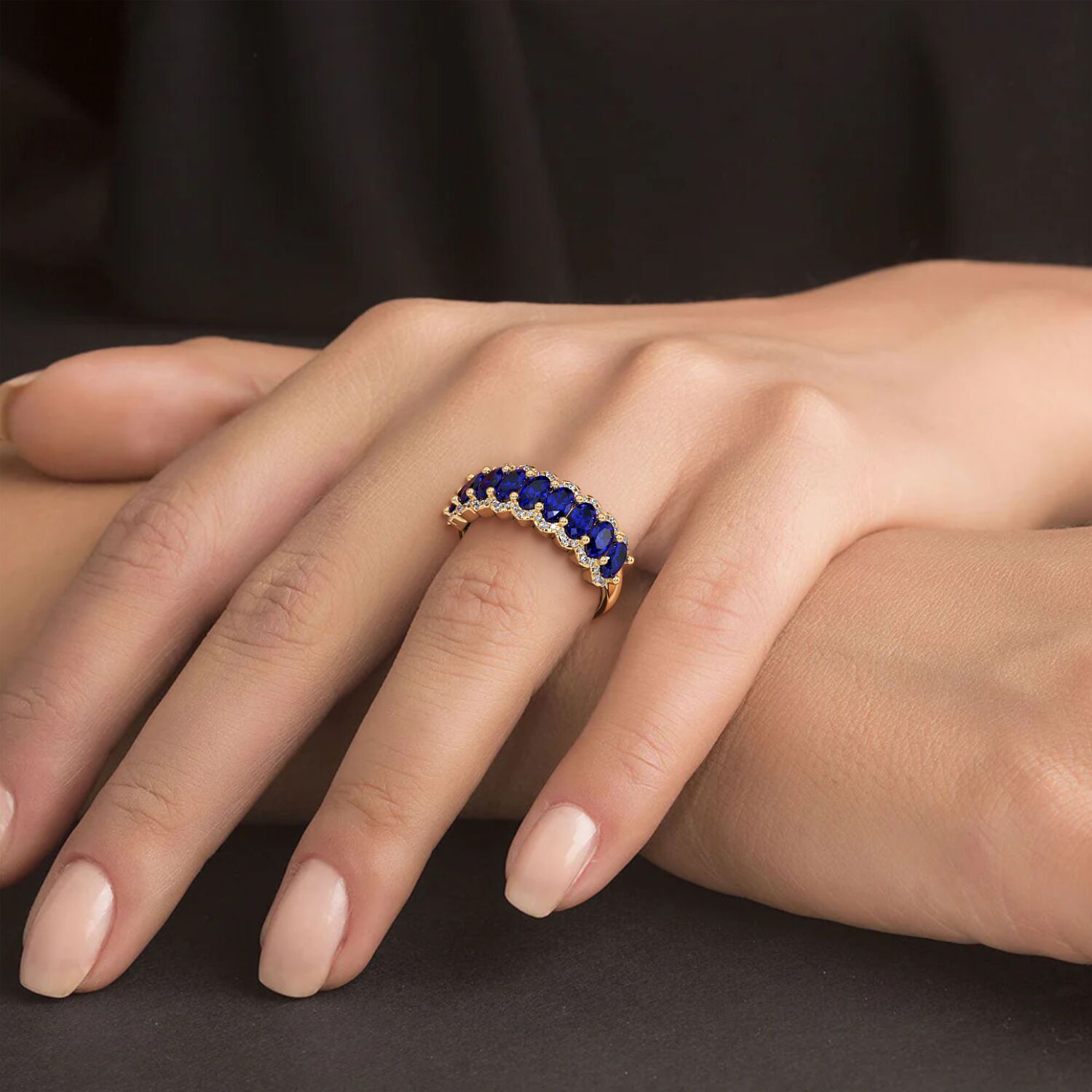 Hand resting on a surface, adorned with a 14k gold ring featuring deep Blue Sapphire stones and small diamonds.