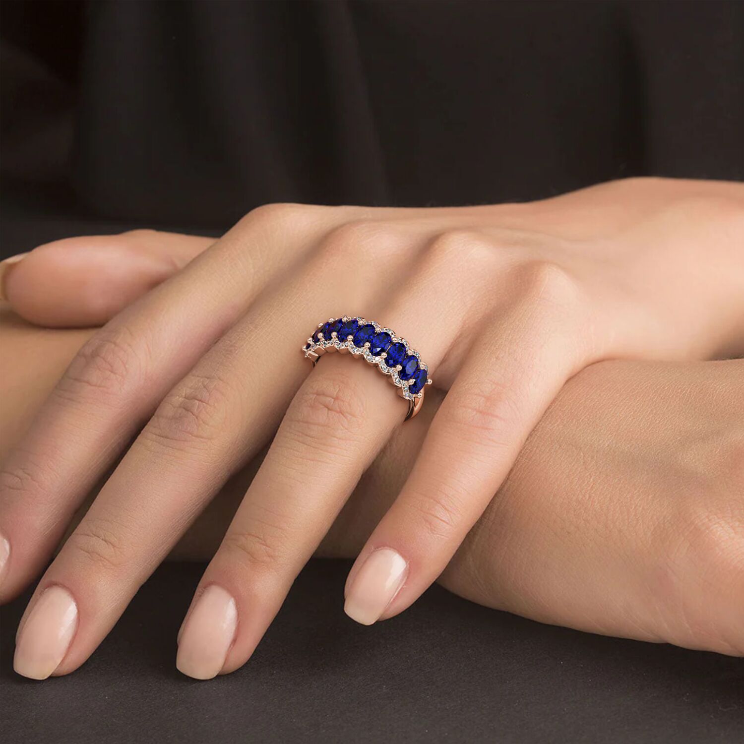 Hand wearing a 14k white gold ring set with deep Blue Sapphire gemstones, gently resting on black fabric.