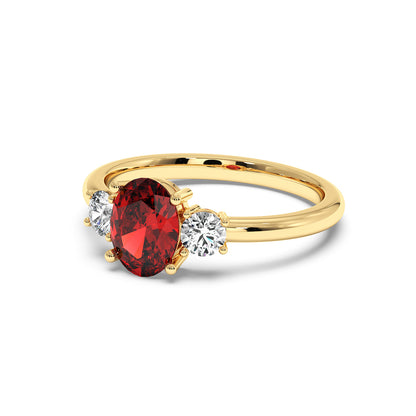 Gold ring with a central red oval ruby flanked by two round diamonds, showcasing an elegant and luxurious design.