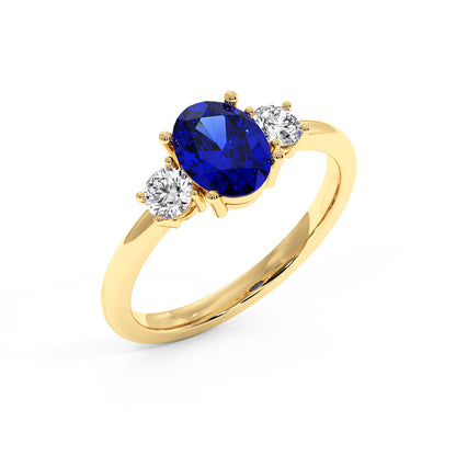 Top view of gold ring with an oval blue sapphire center and two round white diamonds on each side, set against a white background.
