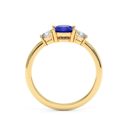 A gold ring with a central blue gemstone flanked by two smaller white gems, featuring an elegant and luxurious symmetrical design.