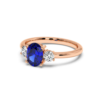 Rose gold 1.75CT oval sapphire ring with blue center gemstone flanked by two round white diamonds. Elegant, classic design.