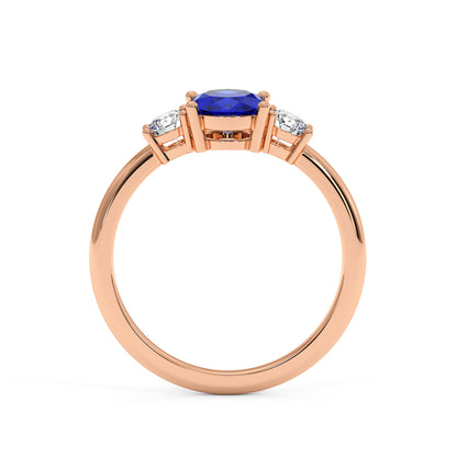 Rose gold 1.75CT oval sapphire ring with blue center stone flanked by two smaller diamonds. Elegant, luxurious design.