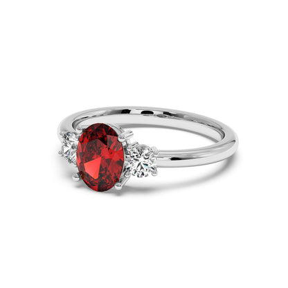 14k white gold oval ruby ring with red center stone flanked by two round clear diamonds. Elegant, luxurious design.