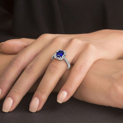 Close-up of a hand wearing a 14k white gold blue sapphire ring encircled by diamonds, resting on a dark surface, exuding elegance.